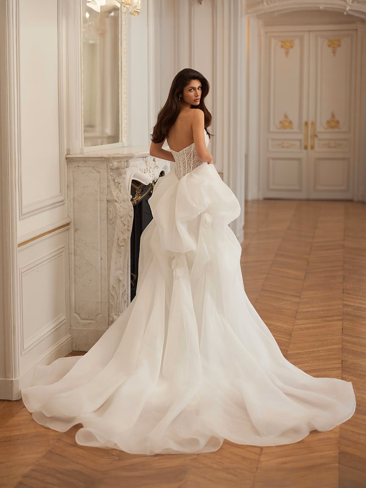 Elegant woman in an opulent, wood-floored room wearing a strapless ivory neckline with a long, flowing train, exudes sophistication and grace Val Stefani REGALIA