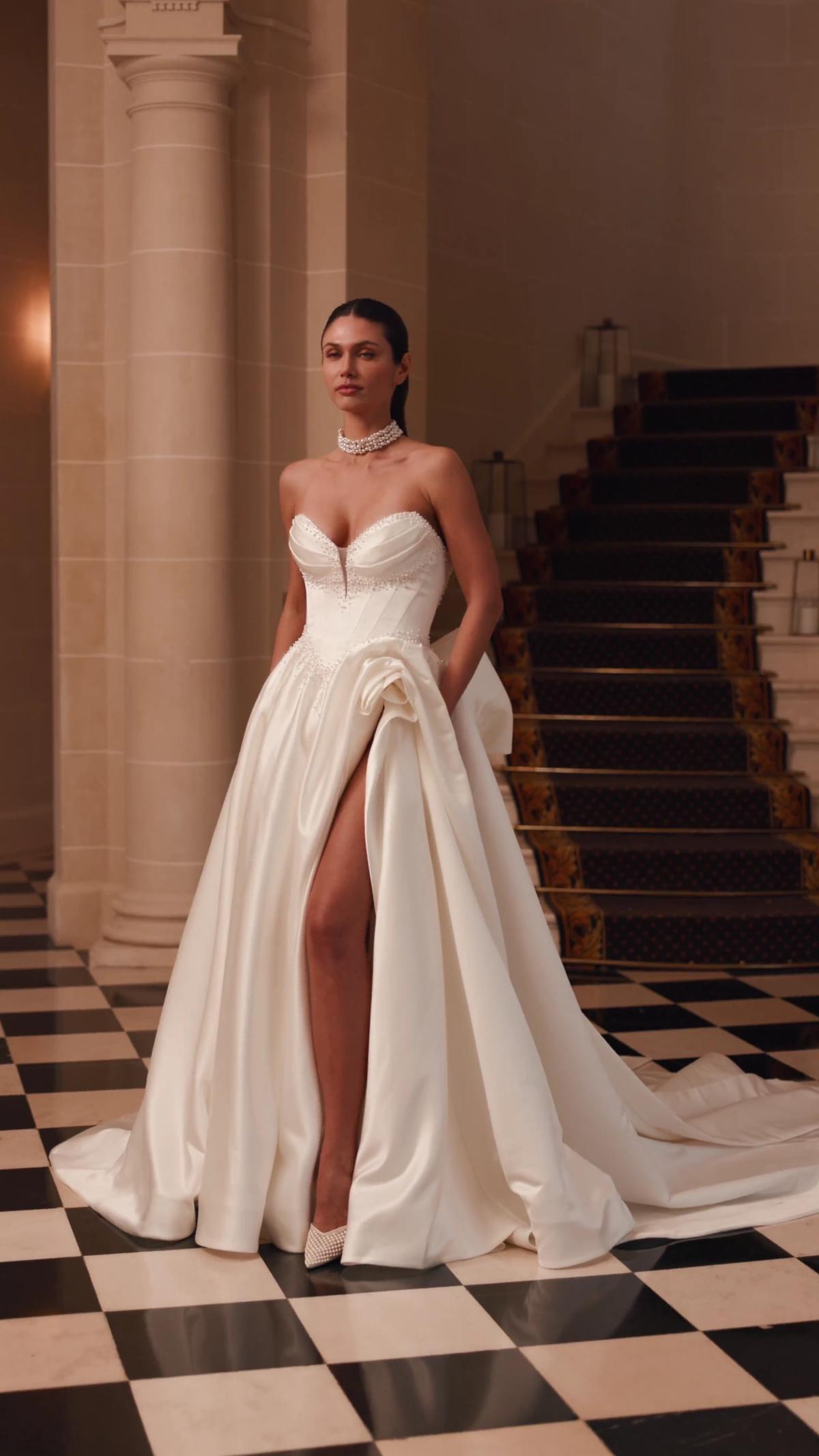 Video of ValStefani ASTRAELIA satin A-line with 3D flower at slit and detachable bow train Video of ValStefani ASTRAELIA satin A-line with 3D flower at slit and detachable bow train